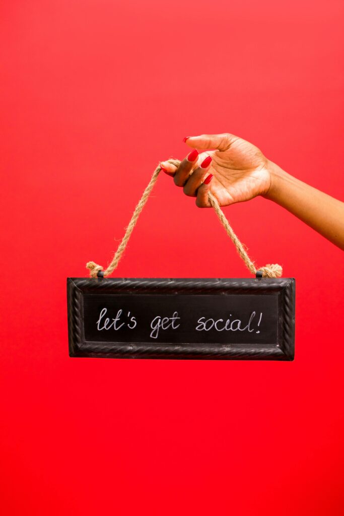 A hand holding a black chalk sign with "let's get social!" written in white chalk, against a vibrant red background.